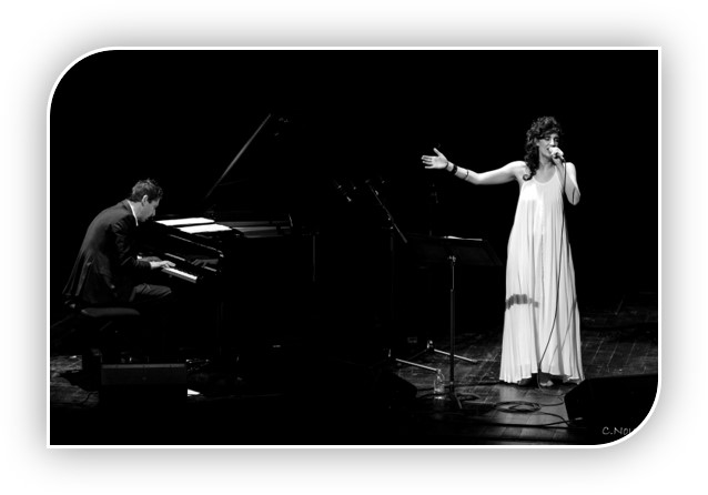 Photo de Aelle qui chante dans une belle robe blanche, micro à la main et de Grégory Ott qui joue du piano