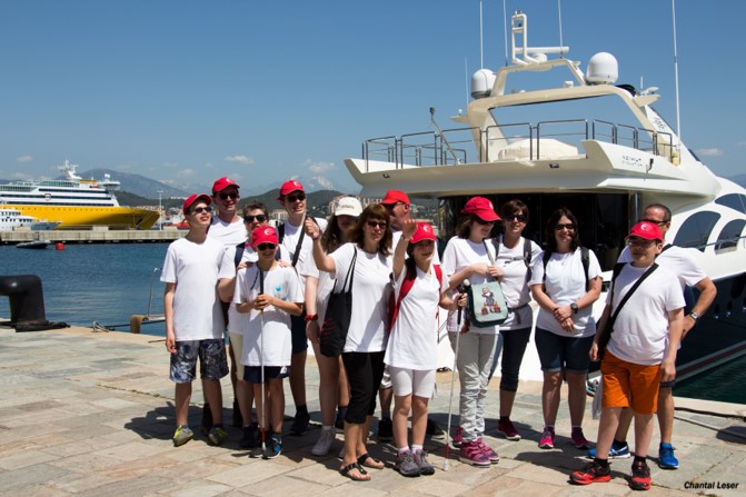 Photo des participants au voyage en Corse devant des bateaux, ils ont tous leur tee-shirt blanc du voyage et la casquette rouge de Visionère