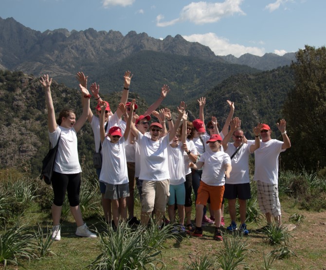 Photo des participants au voyage en Corse devant un paysage de hautes montagnes. Tout le monde lève les bras.