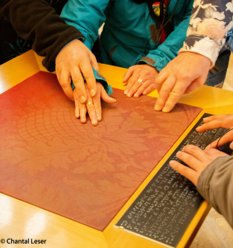 Plusieurs mains touchent une tapisserie du château de Schoenbrunn et lisent du braille