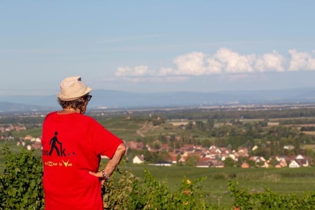 Vue de Chantal de dos, avec son tee-shirt pour les 100 km pour la vue, et qui regarde en direction la plaine