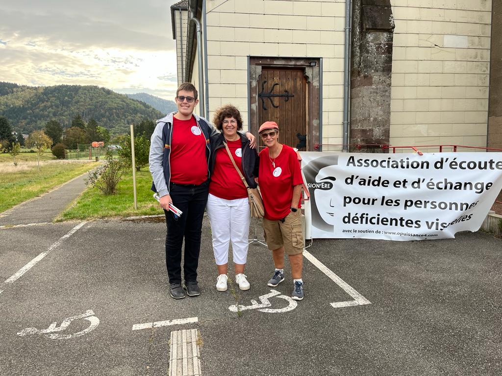 Matthieu, Chantal et Delphine posant à coté de la banderole tendu sur la place de l’Église à Dolleren