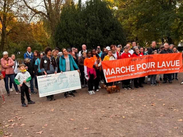 Le groupe de marcheurs prêt à s'élancer pour la marche derrière la banderole de la marche pour la vue et le chèque géant des 10 000 € de l'IRRP pour l'achat du Clarus 500 de Zeiss.