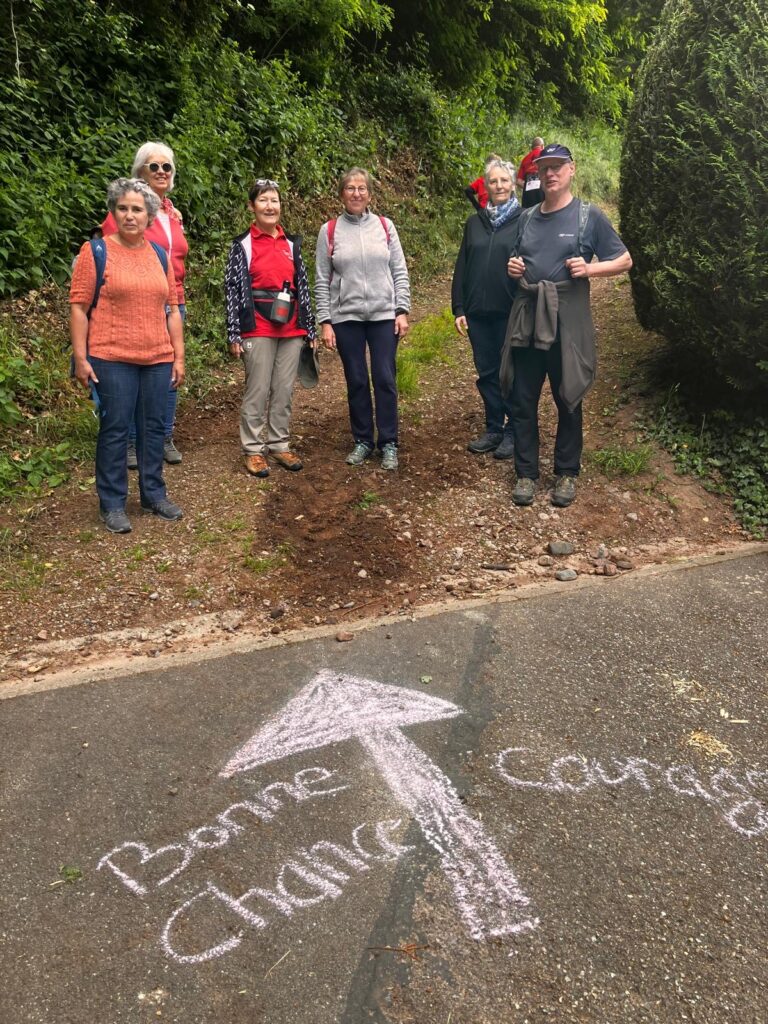Un groupe de marcheurs prend la pose devant un fléchage à la craie et avec bonne chance et courage noté sur la route