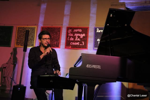 Grégory Ott assis devant son piano, micro à la main en train de s'adresser au public